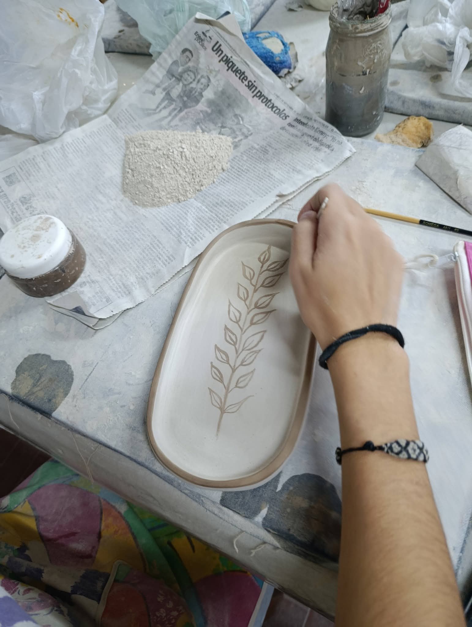 Una mano pintando una ramita sobre una bandeja de cerámica